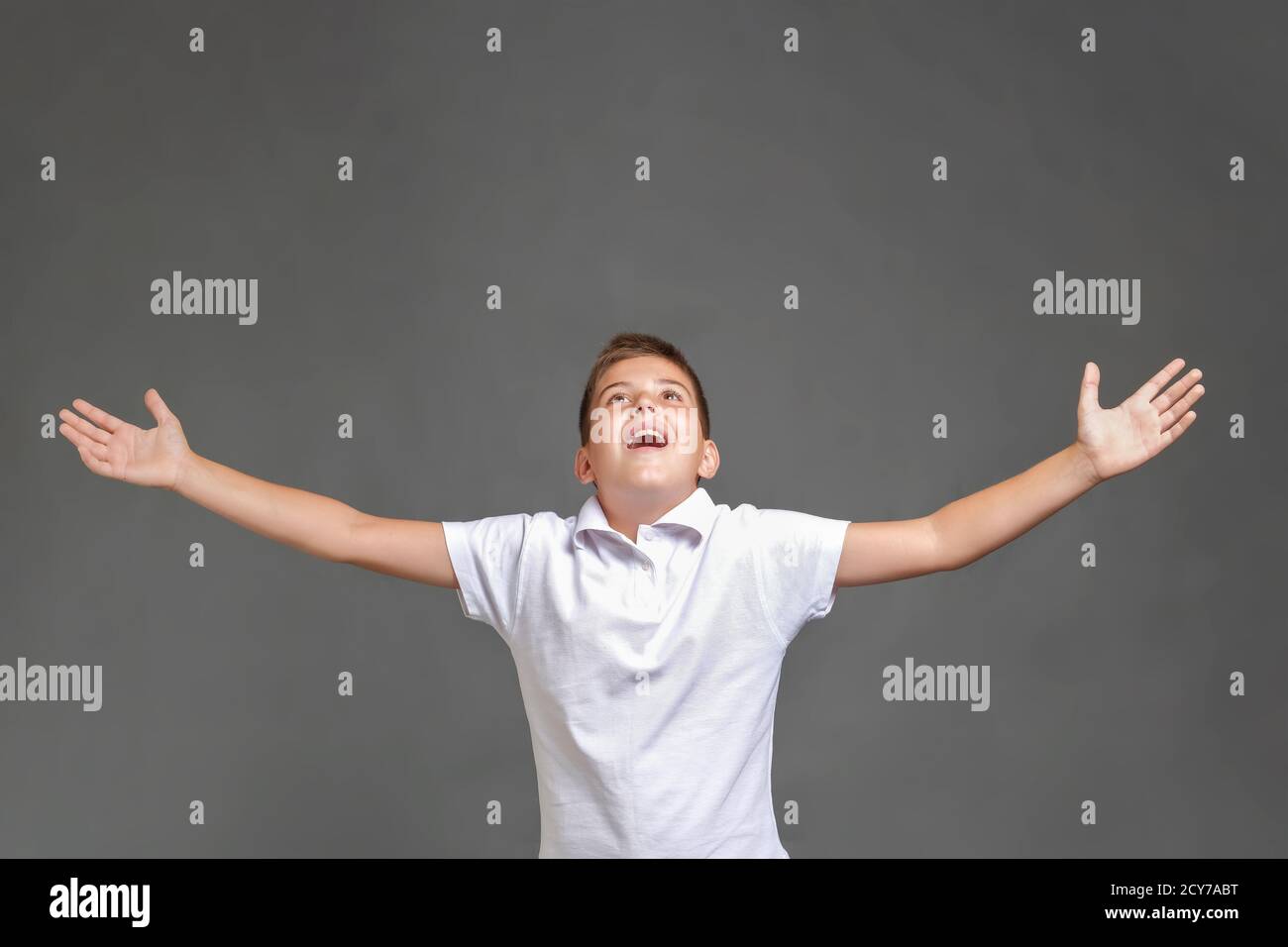 Joyeux garçon avec les bras relevés vers le haut sur fond gris. Banque D'Images