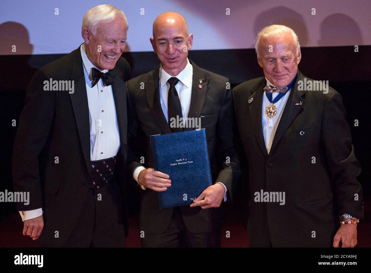 Explorers Club President Alan Nichols (L) and Astronaut Edwin "Buzz" Aldrin  (R) present the Citation of Merit to Amazon CEO and Chairman Jeff Bezos (C)  and the Apollo F-1 Search and Recovery