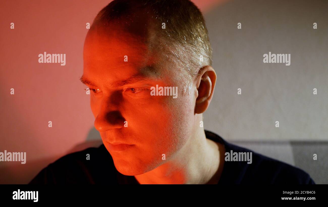 Un jeune homme avec un regard sérieux. Homme froid dans les tons rouges mal sourire Banque D'Images