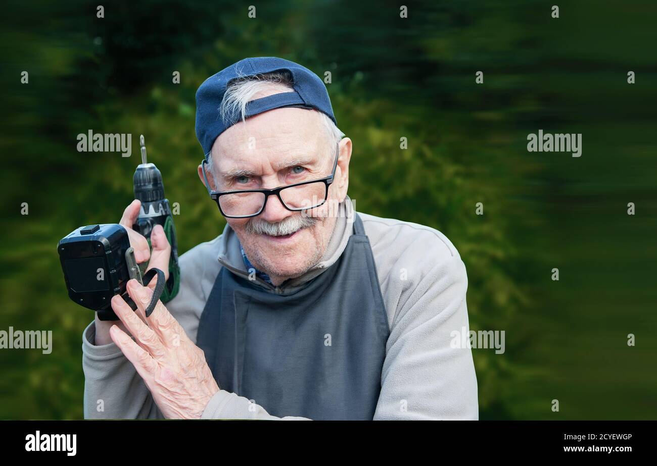 Un vieil homme heureux posant avec une perceuse électrique, souriant. Ancien agriculteur avec un semoir. Copier l'espace Banque D'Images