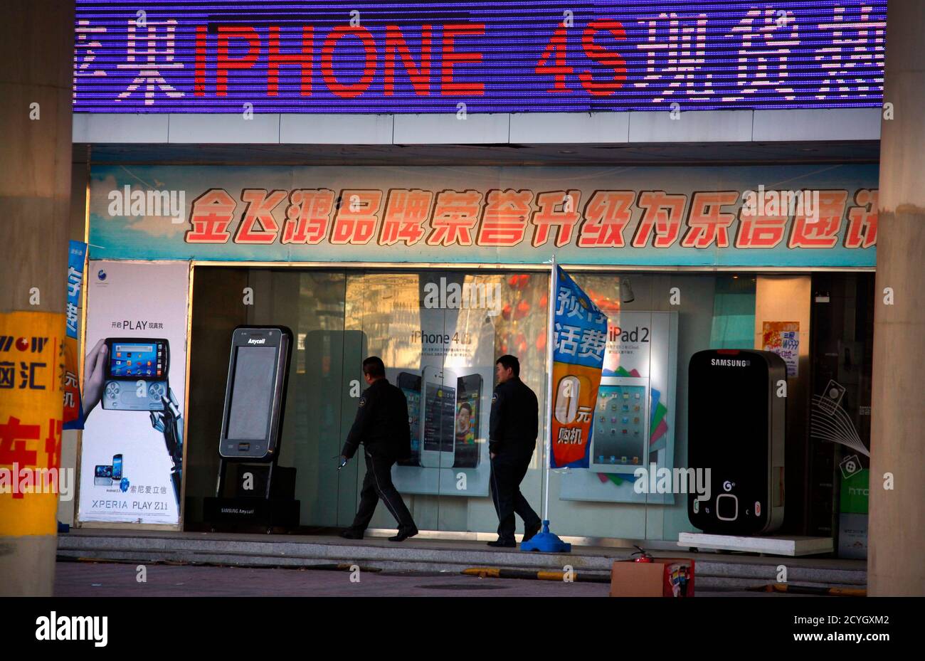 Two security guards walk past an electronics store advertising Apple's  iPhone 4S and iPad2, as well as other phones and hand-held devices, in  central Beijing January 25, 2012. Apple said in a
