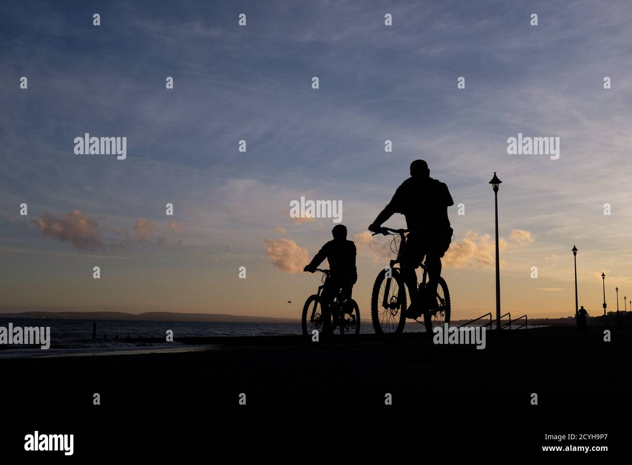 Deux cyclistes se promondent à vélo le long de la promenade juste après le crépuscule, un soir d’août sur la plage à Fisherman’s Walk à Bournemouth. 05 août 2016. Pho Banque D'Images