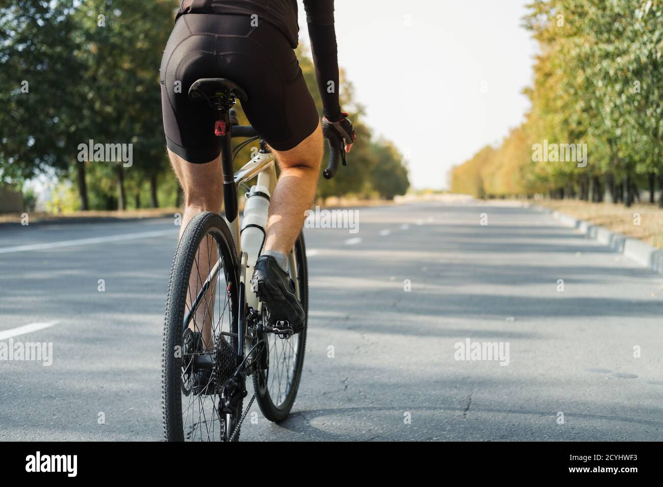 Homme sur un vélo de gravier sur la route, vue arrière. Jambes d'un cycliste à vélo moderne en plein air Banque D'Images