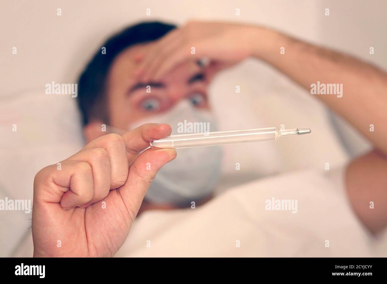 homme dans le masque d'un virus avec thermomètre dans les mains. Épidémie de coronovirus. Température, thermomètre. L'homme est surpris par la température élevée Banque D'Images