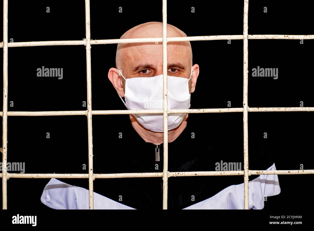 concept de restriction et de quarantaine pandémique homme bald d'âge moyen dans un masque d'hygiène médical derrière des barres de fer Banque D'Images