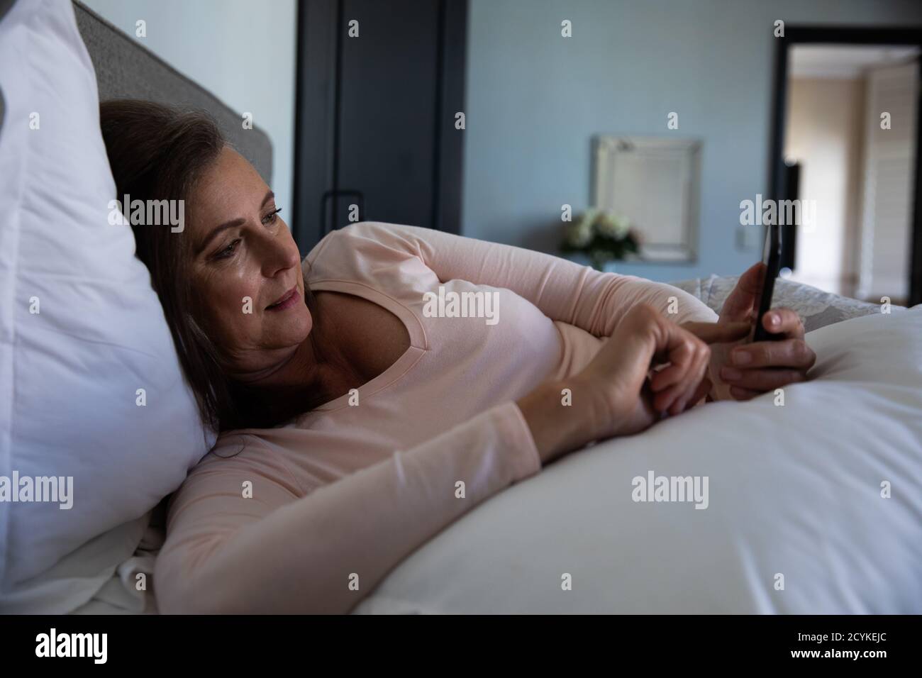Femme âgée utilisant un smartphone dans le lit à la maison Banque D'Images