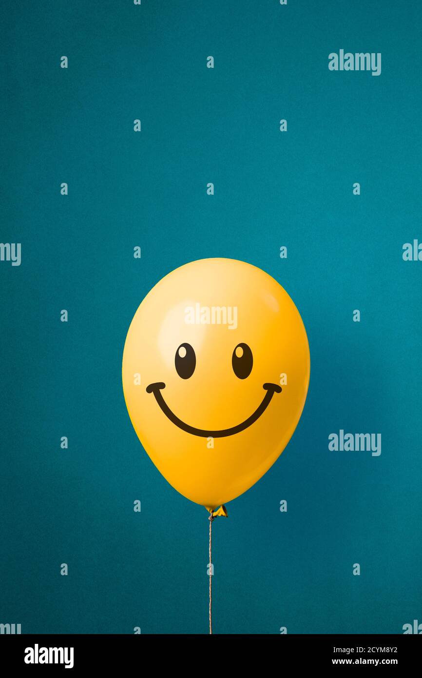Photo d'un ballon jaune avec un visage heureux sur fond bleu. La joie et le bonheur Banque D'Images