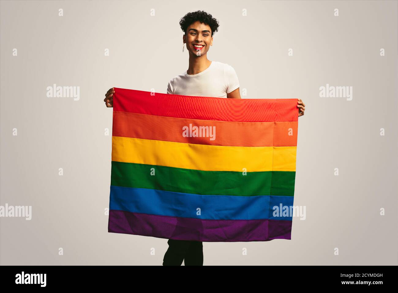 Homme gay souriant avec drapeau de fierté. Homme fluide de genre tenant un drapeau lgbt sur fond blanc. Banque D'Images