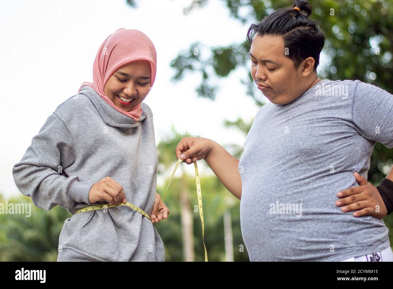 Deux personnes, une femme musulmane et un gros homme, proportionnel et de poids excessif, asiatique homme de poids excessif regarder l'envie de sa femme musulmane corps mince à l'extérieur ci Banque D'Images