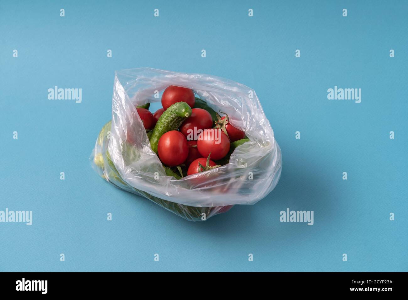 Vue avant concombres et tomates dans un sac en plastique sur fond bleu. L'image montre la nocivité de l'utilisation de sacs de stockage d'aliments artificiels. Image horizontale Banque D'Images