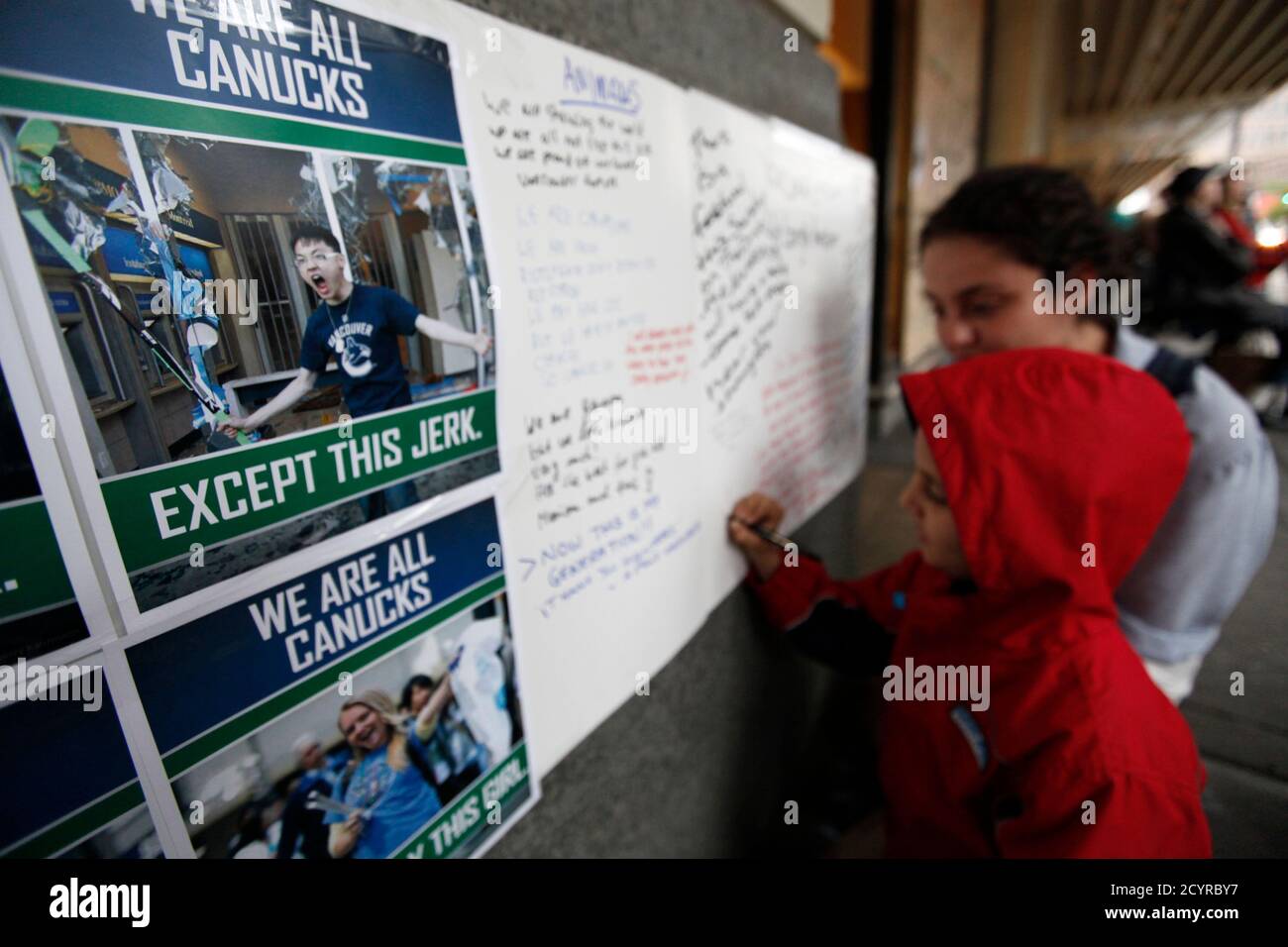 A boy writes messages outside a damaged store next to pictures showing  scenes of the riot after the NHL Stanley Cup finals in downtown Vancouver,  British Columbia June 17, 2011. The riots