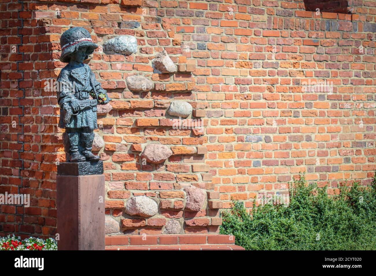 Monument de petit garçon insurgé dans un casque et des bottes allemands surdimensionnés, participant au soulèvement de Varsovie en 1944 contre la brique rouge des murs de la ville médiévale Banque D'Images