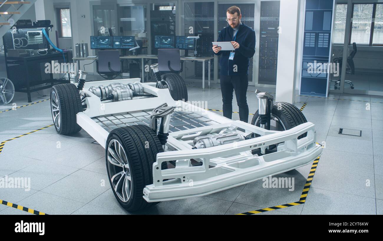 Ingénieur avec des lunettes et Beard scanne le prototype de châssis de voiture électrique avec roues, batteries et moteur avec un logiciel de réalité augmentée sur une tablette Banque D'Images