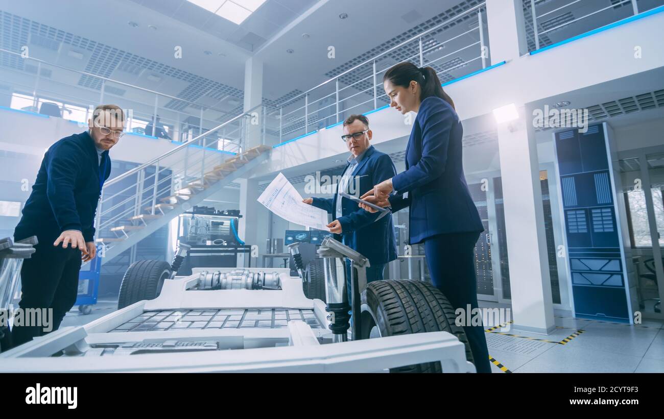 Ingénieurs de conception automobile regardant les dessins techniques d'un prototype de châssis de voiture électrique. Dans le concept d'installation de laboratoire d'innovation cadre de véhicule Banque D'Images