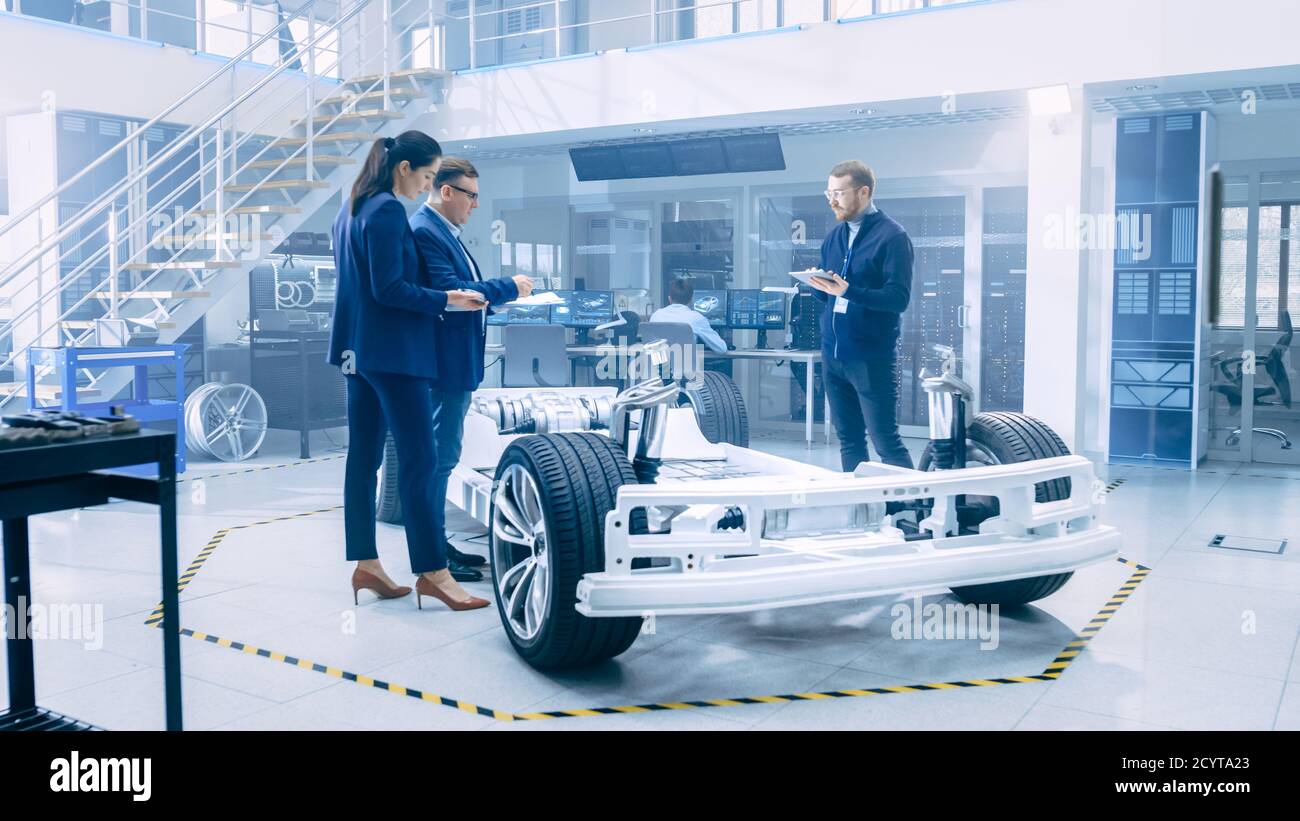 Ingénieurs de conception automobile regardant les dessins techniques d'un prototype de châssis de voiture électrique. Dans le concept d'installation de laboratoire d'innovation cadre de véhicule Banque D'Images