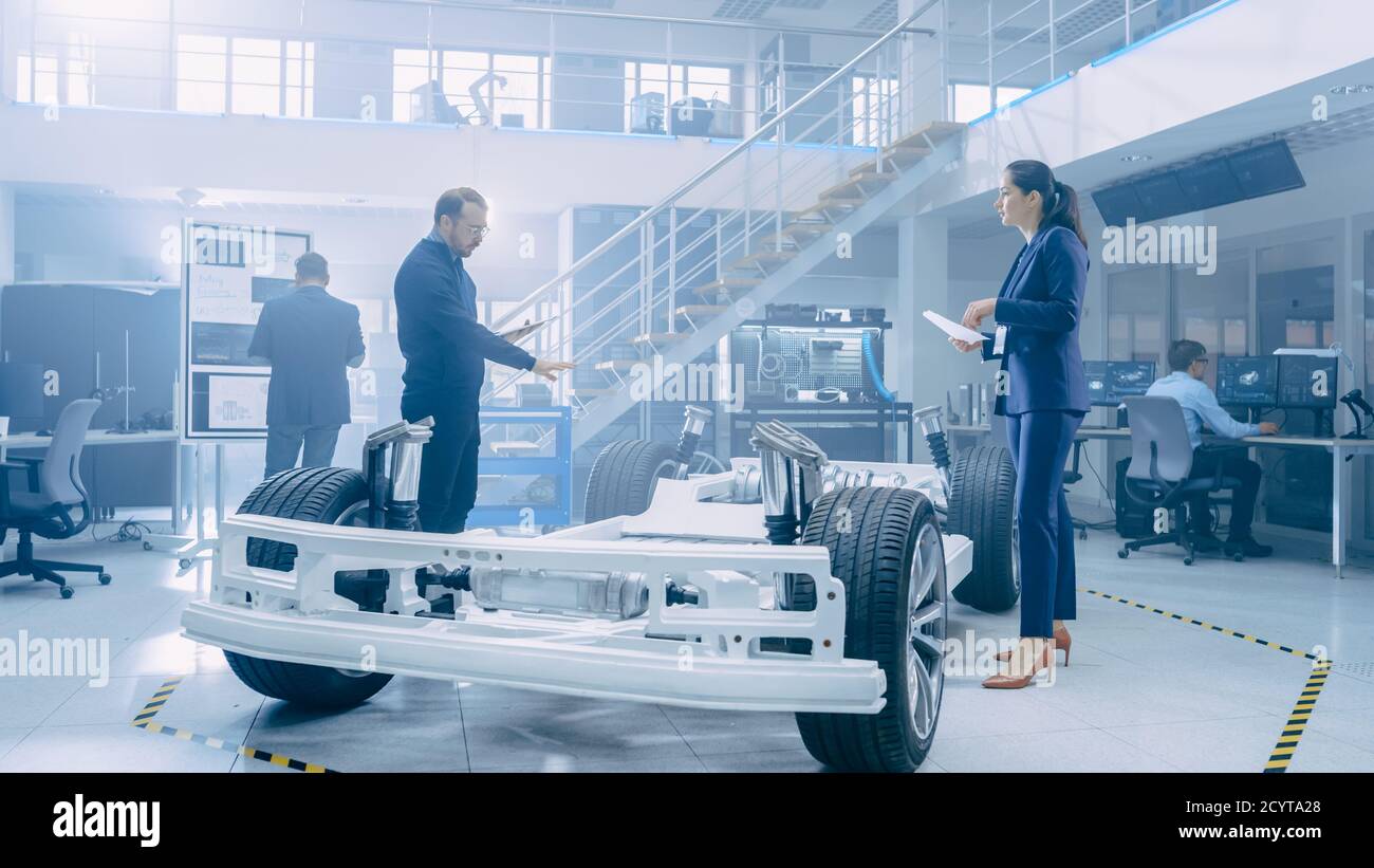 Ingénieurs de conception automobile regardant les dessins techniques d'un prototype de châssis de voiture électrique. Dans le concept d'installation de laboratoire d'innovation cadre de véhicule Banque D'Images