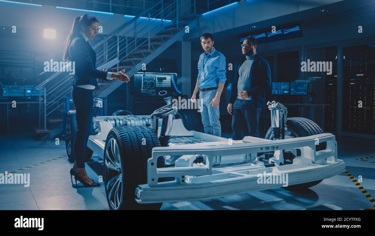 Équipe internationale d'ingénieurs concepteurs d'automobiles discutant de la conception de prototype de voiture électrique autonome. Châssis de plateforme de véhicule avec roues Banque D'Images