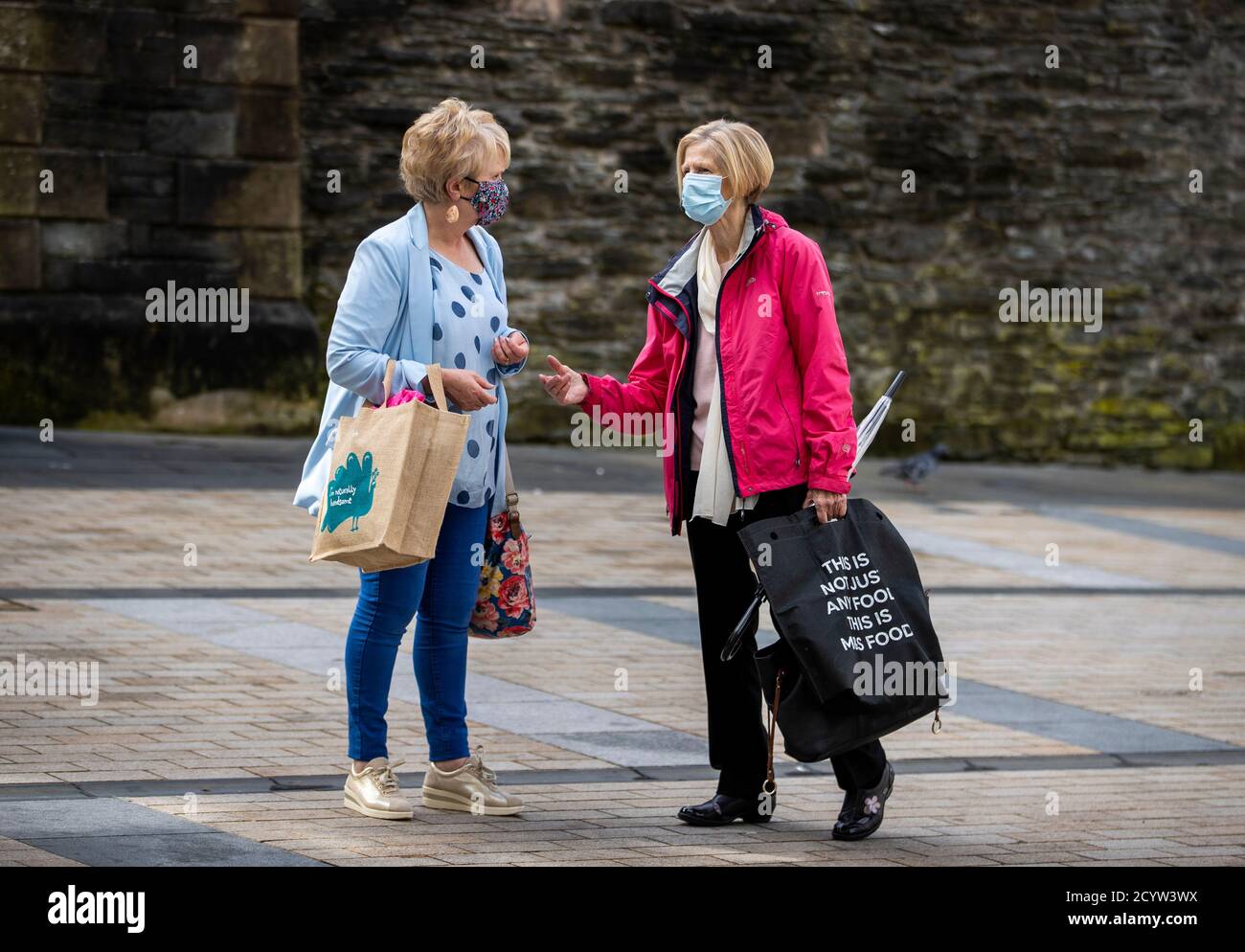 Deux femmes chatent en portant des masques et en tenant des sacs à provisions réutilisables à Derry City. Il a été annoncé que les pubs, les cafés, les restaurants et les hôtels de la région du conseil de Derry et Strabane seront soumis à de nouvelles restrictions pour essayer de freiner la propagation de Covid-19. Banque D'Images