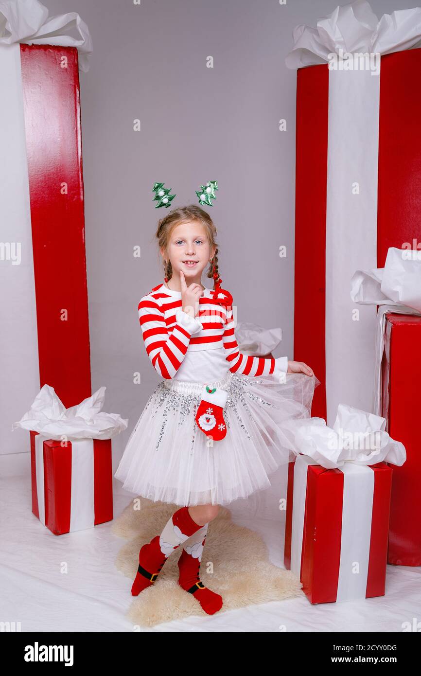 Belle petite fille dans un costume de fête sur le fond de grandes boîtes-cadeaux rouges sur un fond blanc. Fête du nouvel an 2021 con Banque D'Images