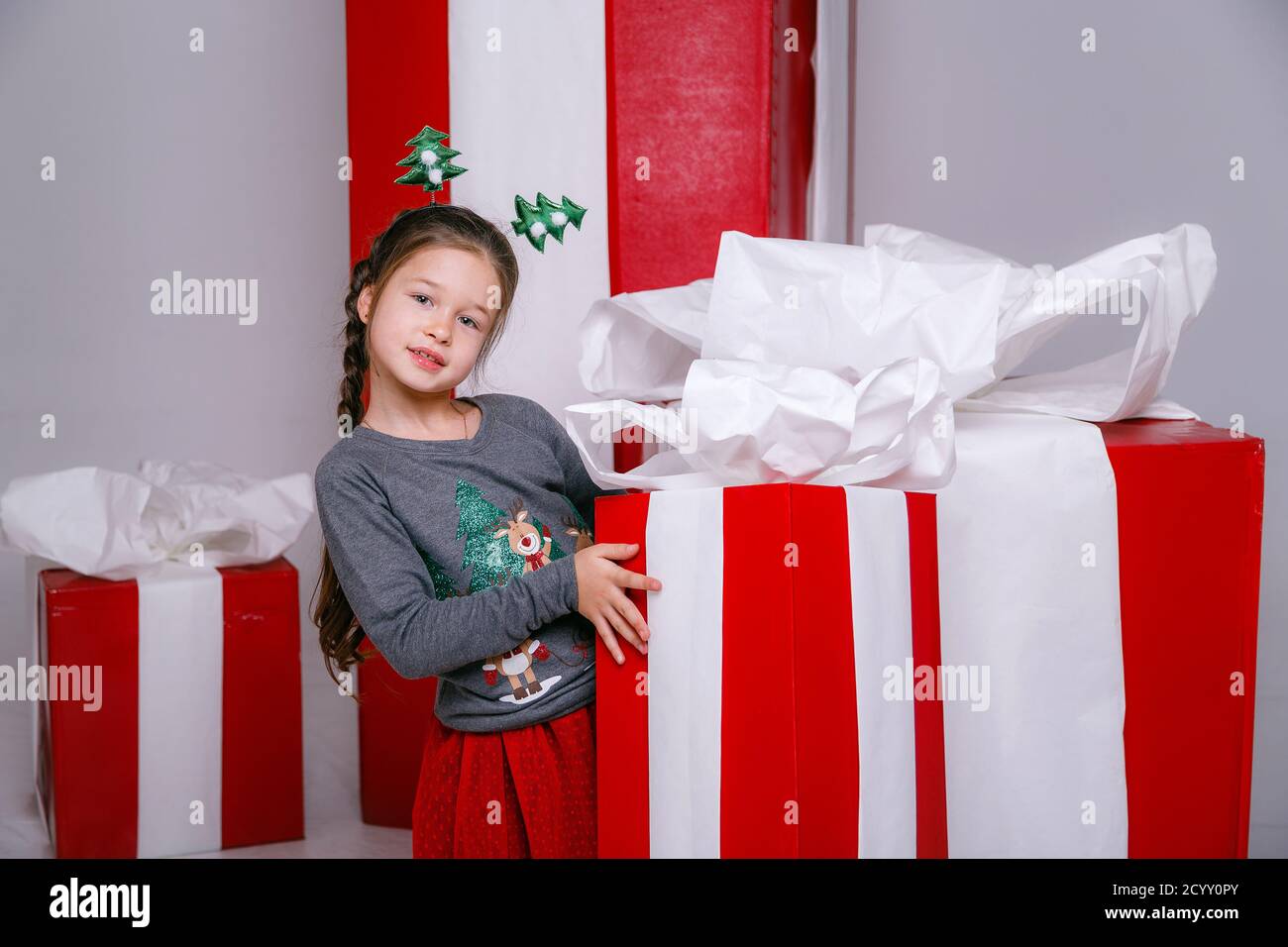 Belle petite fille dans un costume de fête sur le fond de grandes boîtes-cadeaux rouges sur un fond blanc. Fête du nouvel an 2021 con Banque D'Images