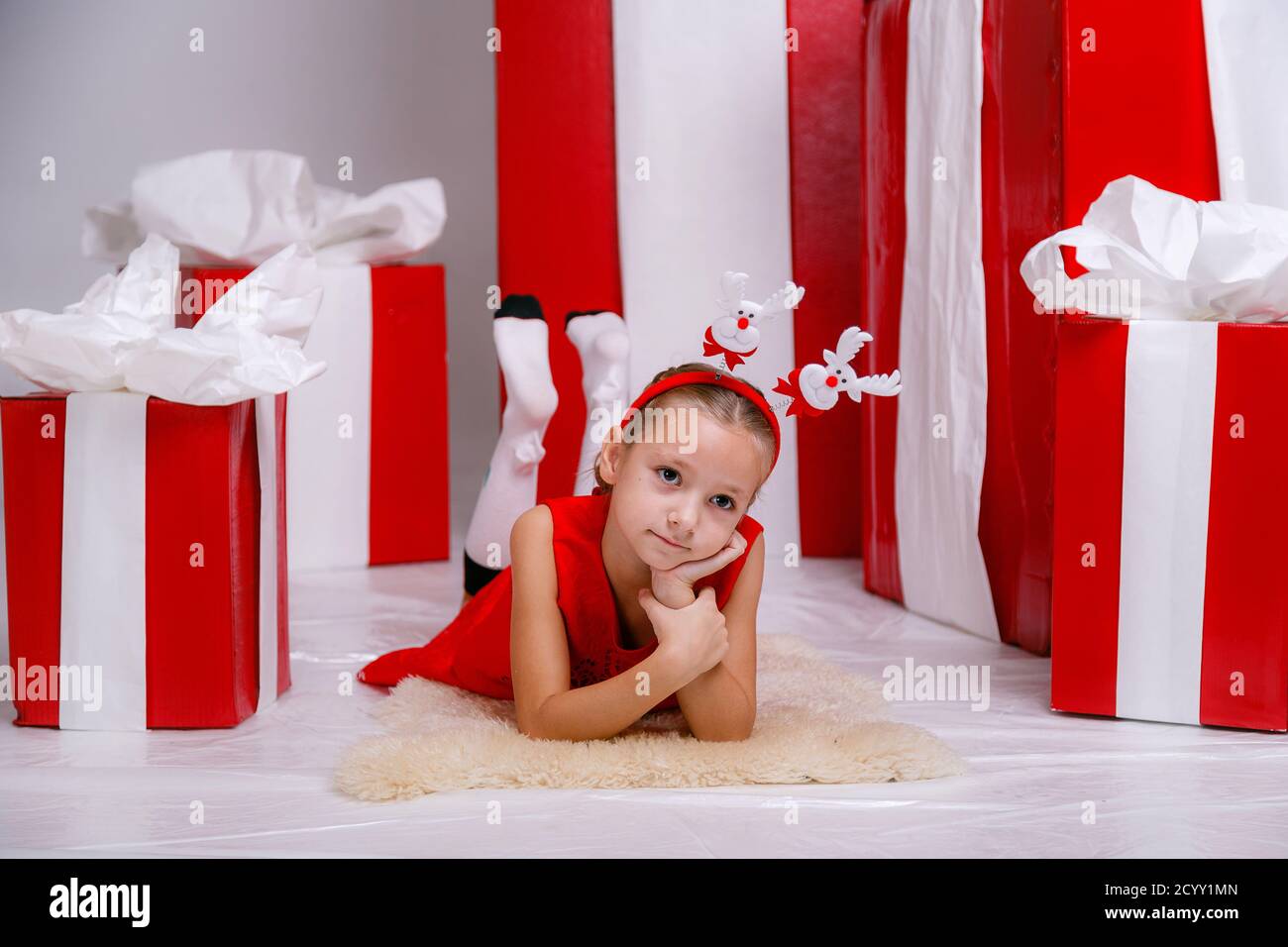 Belle petite fille dans un costume de fête sur le fond de grandes boîtes-cadeaux rouges sur un fond blanc. Fête du nouvel an 2021 con Banque D'Images