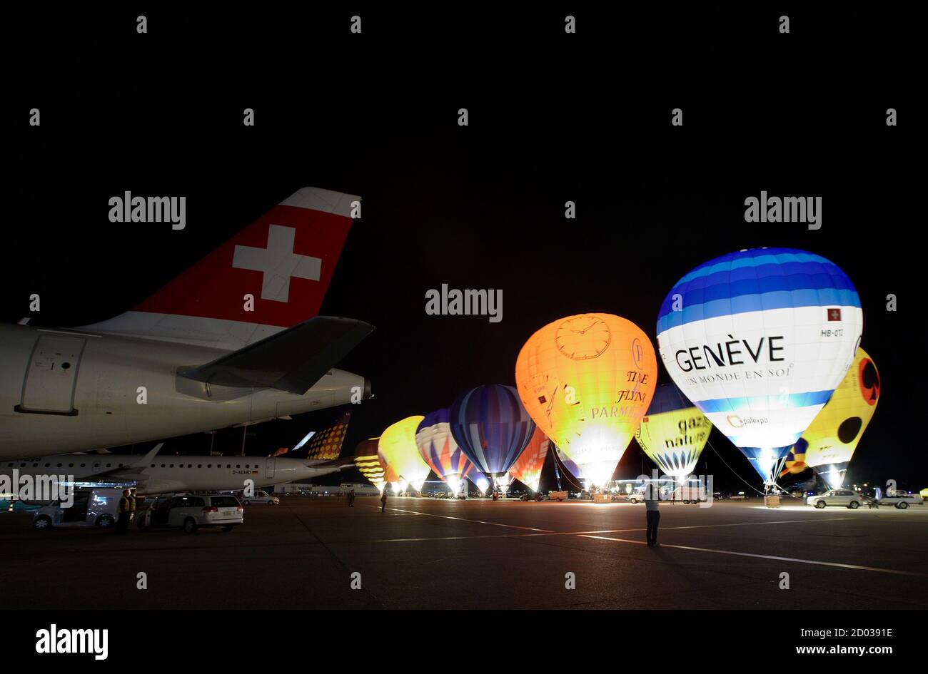Les Balloonistes gonflent leurs ballons à air chaud à côté d'un avion de  compagnie aérienne suisse lors de la lueur nocturne du sixième Festival  Montgolfiades à l'aéroport international de Cointrin à Genève