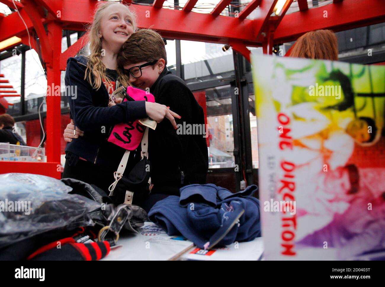 Eleven-year-olds Julia DeRosa and Teresa Levine (R) hug each other during  the opening of global pop music sensation One Direction's exclusive 1D  World pop-up retail store at Faneuil Hall Marketplace in Boston,