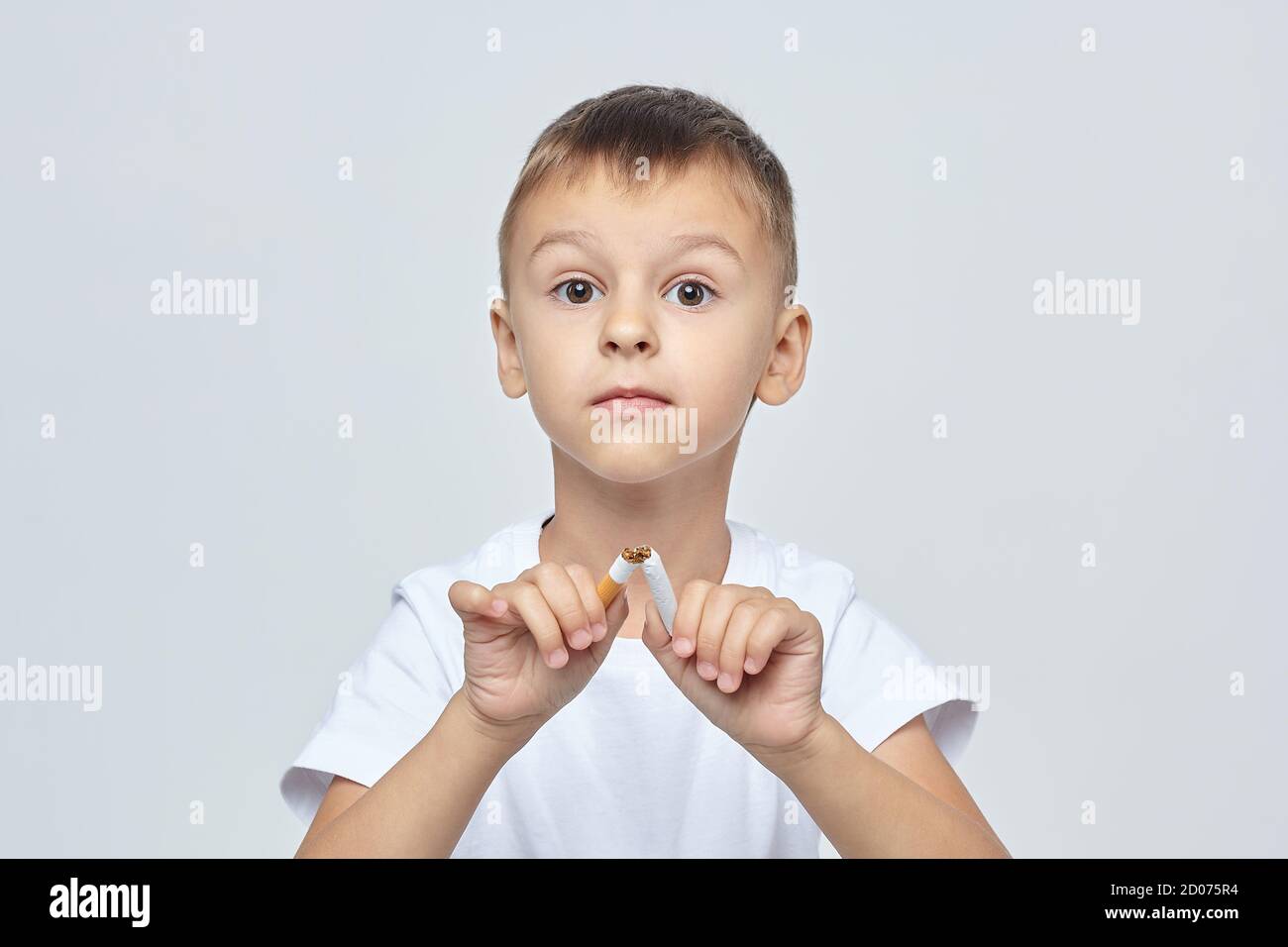 un petit garçon regarde la caméra et casse une cigarette. Banque D'Images