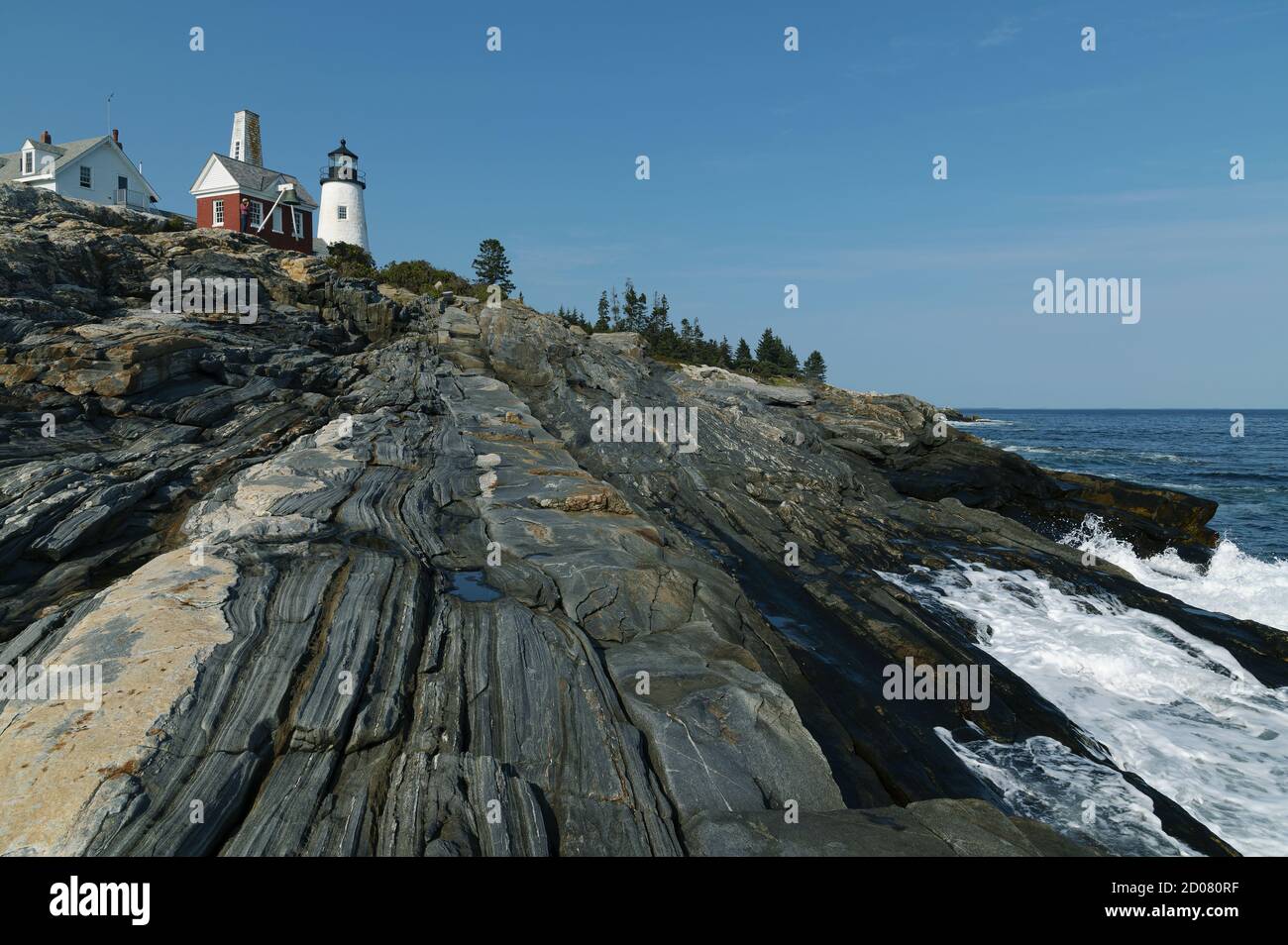 Les vagues se brisent le long de la côte rocheuse. Le phare de Pemaquid point est situé au-dessus de formations rocheuses métamorphiques uniques qui sont une attraction préférée. Banque D'Images