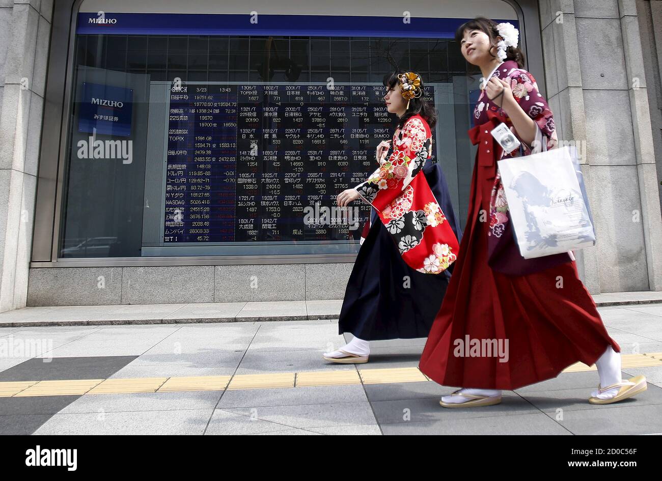 Les femmes portant Hakama, ou kimono traditionnel japonais, marchent devant  un panneau électronique, montrant les différents prix des actions, en  dehors d'une maison de courtage à Tokyo, le 23 mars 2015. Les