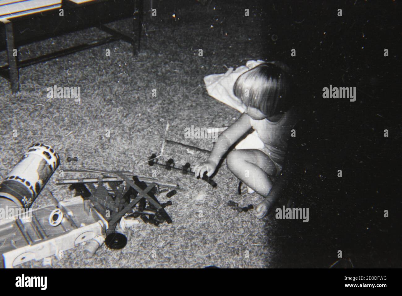 Belle photographie en noir et blanc vintage des années 1970 d'une petite fille jouant sur le sol du salon. Banque D'Images