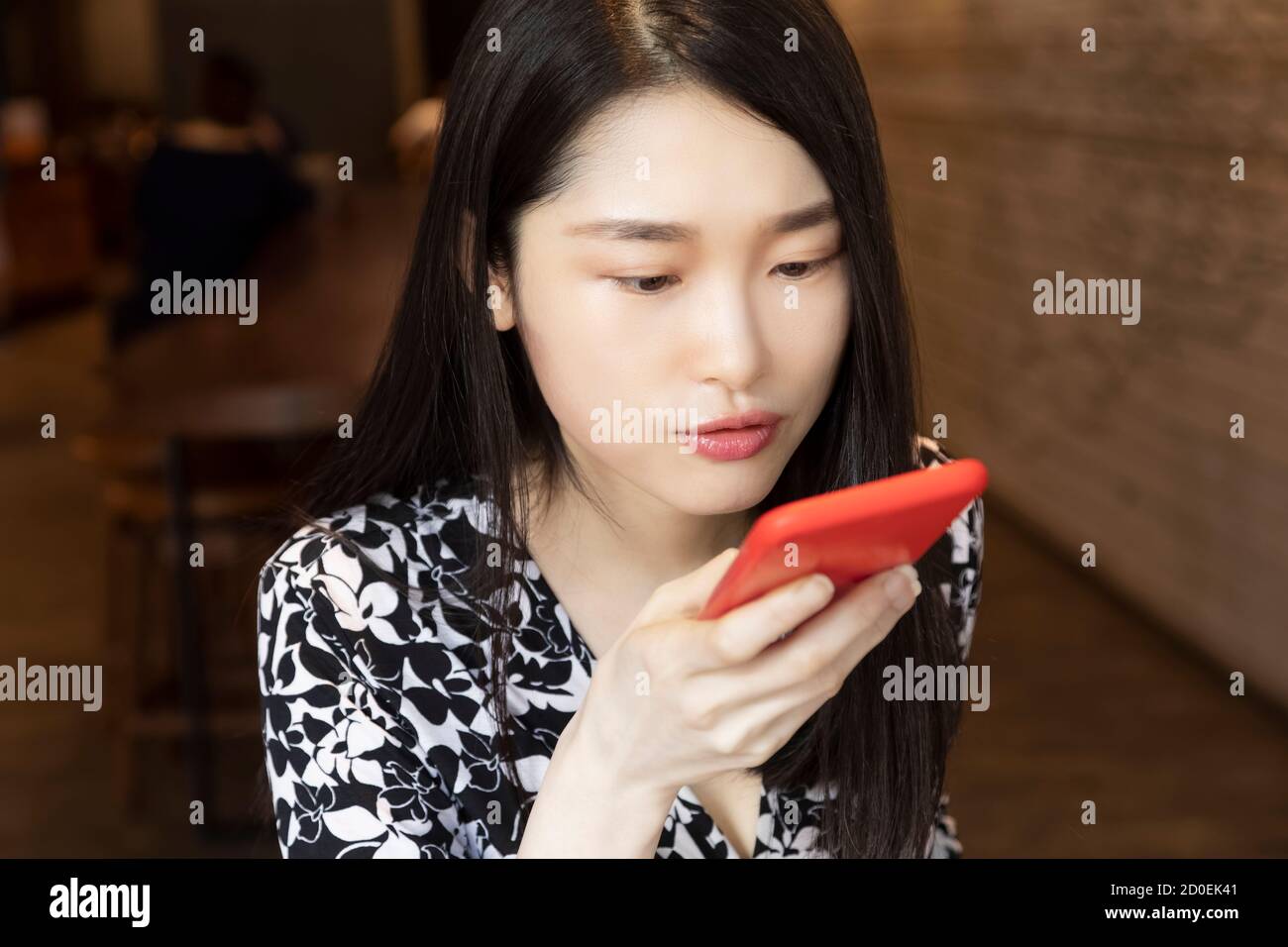 Une femme chinoise américaine profondément pensée en utilisant un rouge intelligent téléphone dans un café Banque D'Images