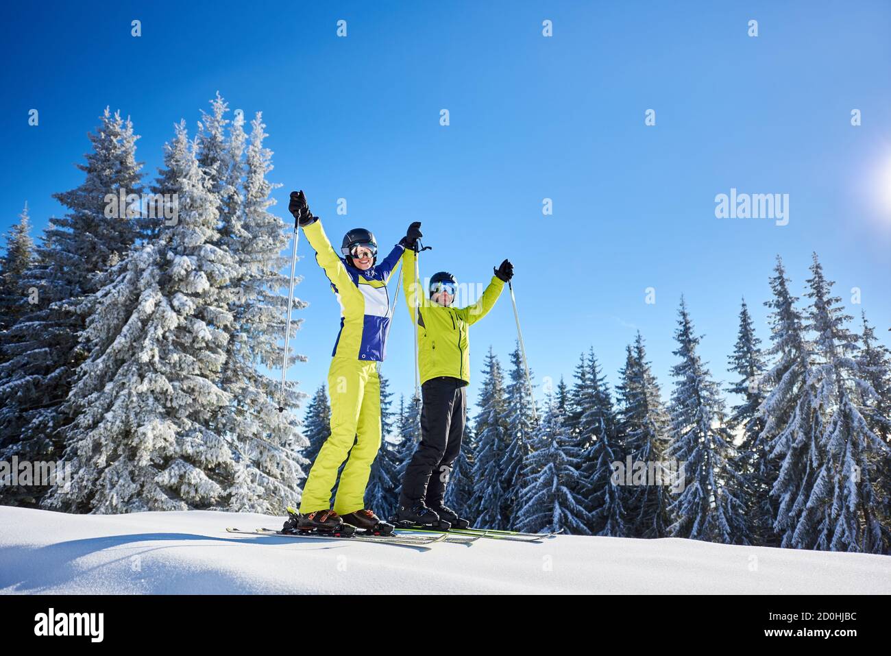 Femme et homme souriants à skis avec bâtons de ski dans les mains. Couple exultant à la station de ski par beau temps d'hiver. Pente boisée enneigée. Ciel bleu clair avec espace de copie. Instantané à partir d'un angle faible. Banque D'Images