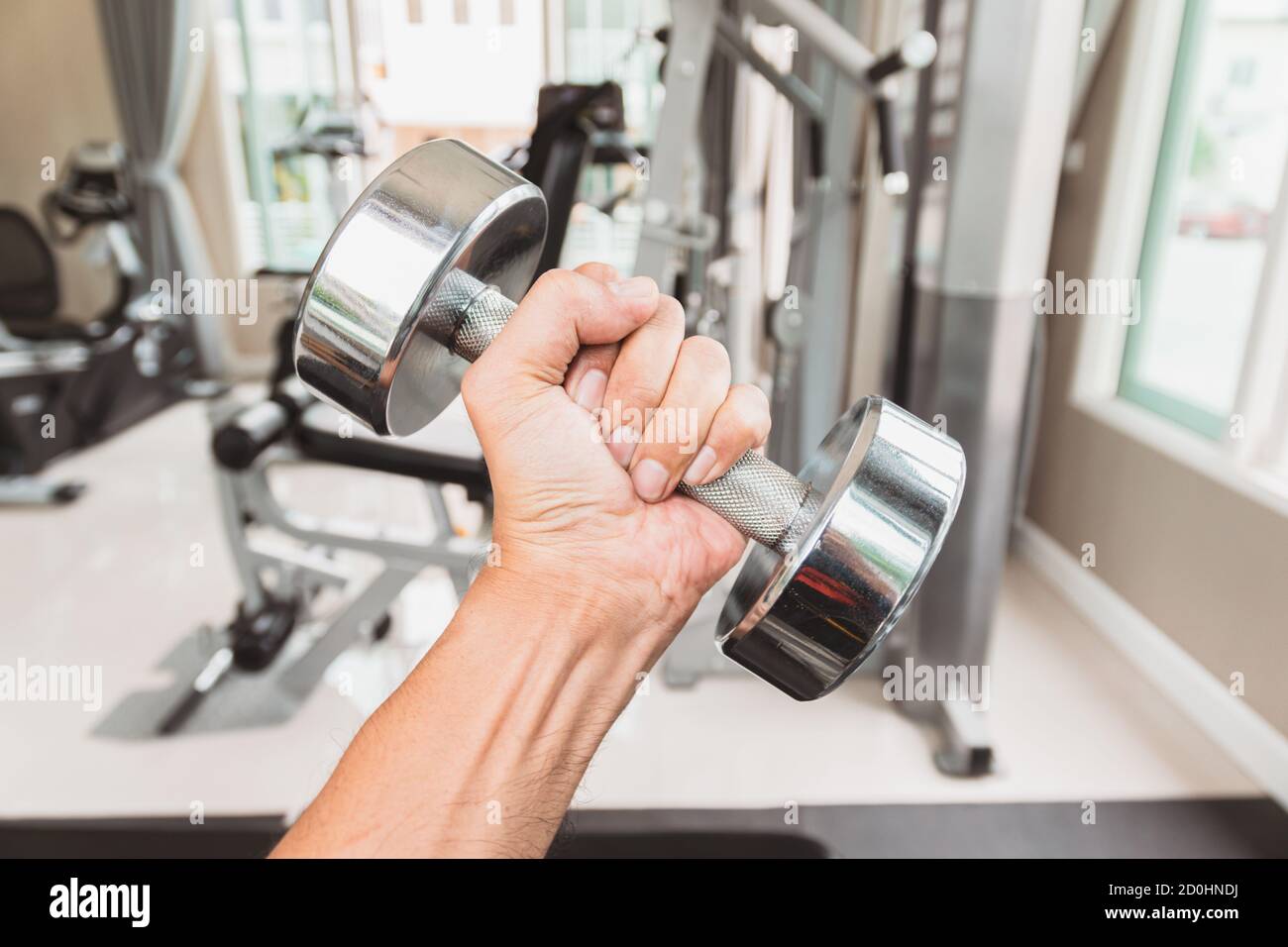 Gros plan la main d'un homme tient une haltère avec sa main gauche dans la salle de gym, concept pour l'exercice et les soins de santé. Banque D'Images