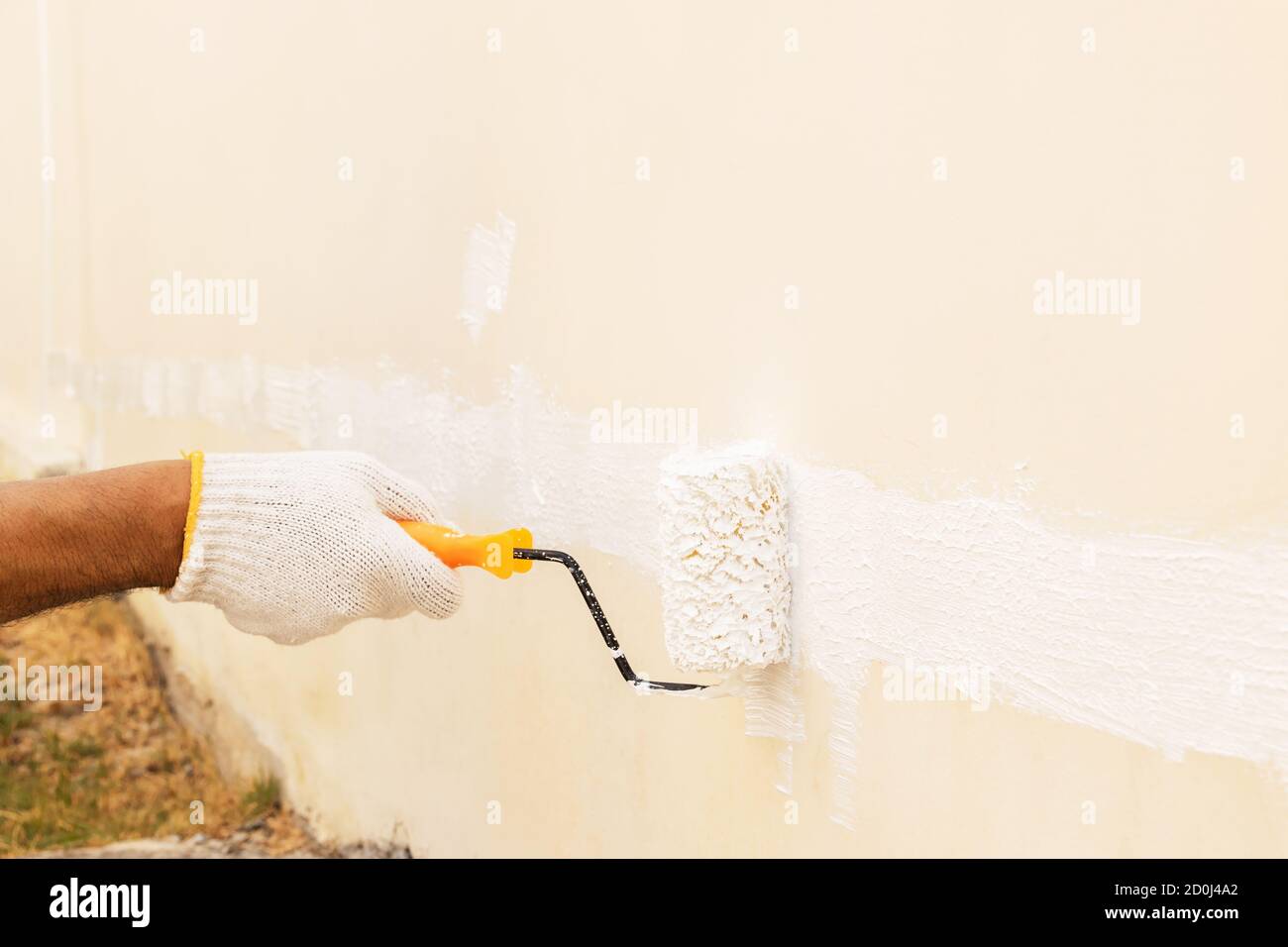 Gros plan à la main en portant des gants en tissu blanc, en utilisant un rouleau pour peindre de la couleur blanche sur le mur en béton. Banque D'Images Gros plan à la main en portant des gants en tissu blanc, en utilisant un rouleau pour peindre de la couleur blanche sur le mur en béton. Banque D'Images