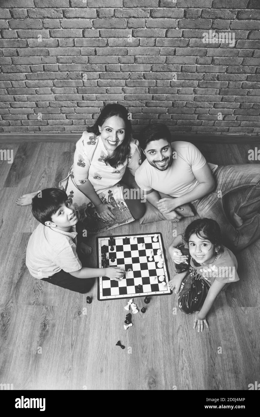 Jeune famille indienne de quatre jeux de société comme les Échecs, le Ludo ou le snack et l'échelle à la maison en quarantaine Banque D'Images