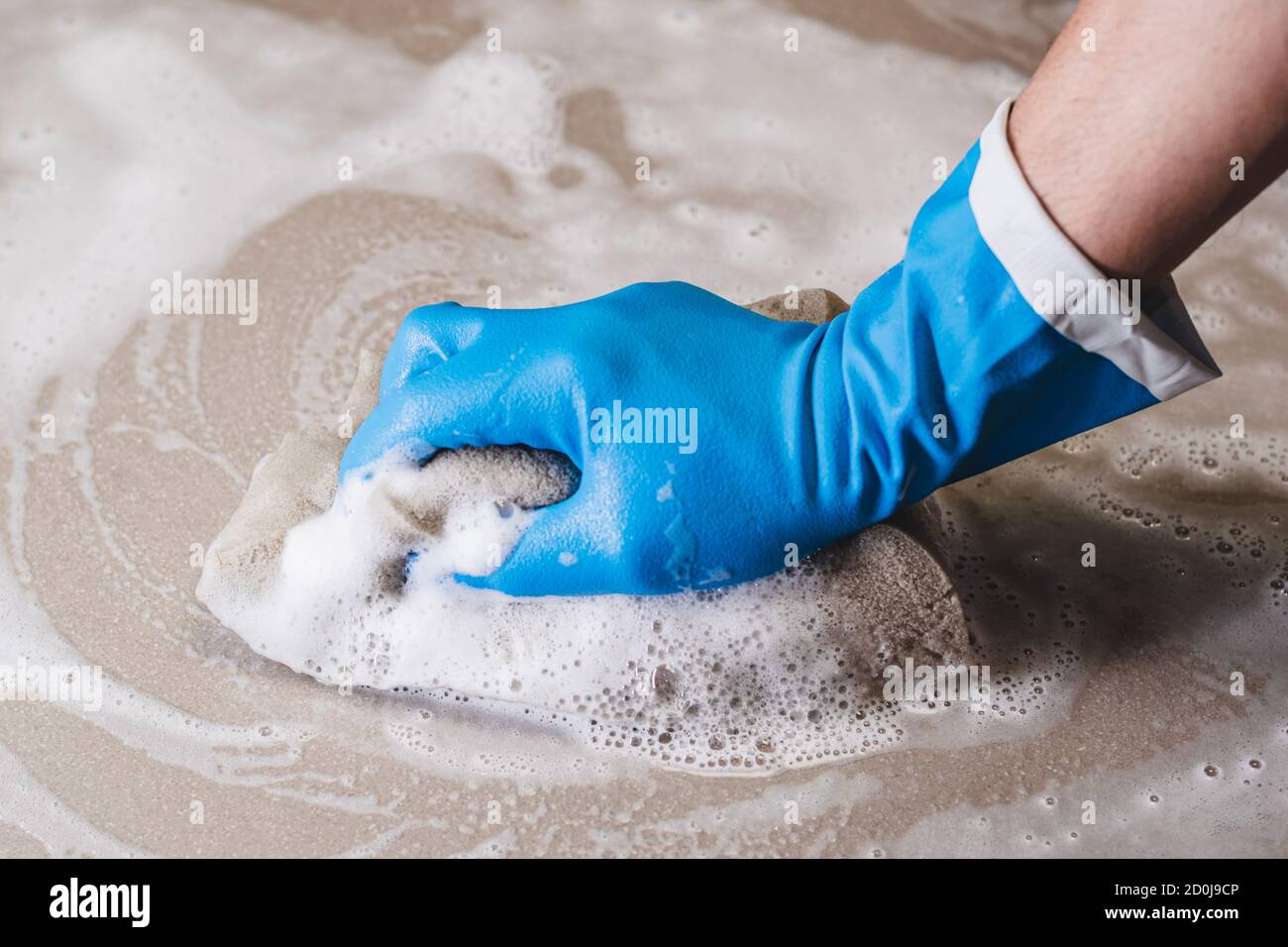 La main de l'homme portant des gants en caoutchouc bleu utilise une éponge pour nettoyer le sol carrelé. Banque D'Images La main de l'homme portant des gants en caoutchouc bleu utilise une éponge pour nettoyer le sol carrelé. Banque D'Images
