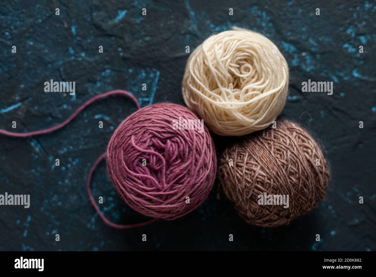 Trois boules de couleur beige rose brun pelote de fil de laine pour crochet et tricoter sur le béton de mastic bleu foncé. Mettre à plat l'image avec de l'espace pour le texte. Banque D'Images
