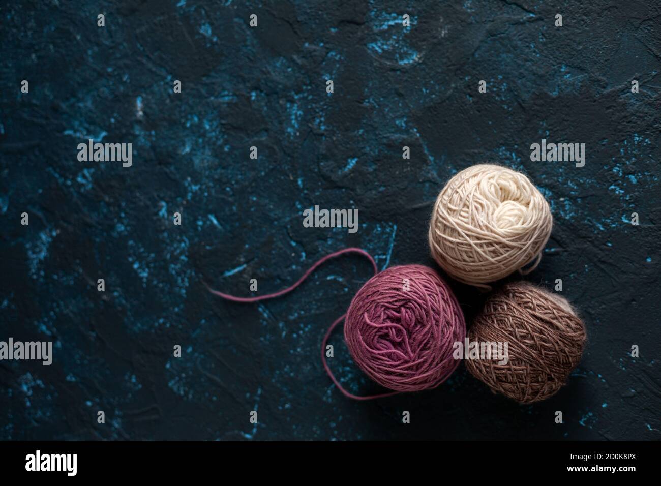 Trois boules de couleur beige rose brun pelote de fil de laine pour crochet et tricoter sur le béton de mastic bleu foncé. Mettre à plat l'image avec de l'espace pour le texte. Banque D'Images