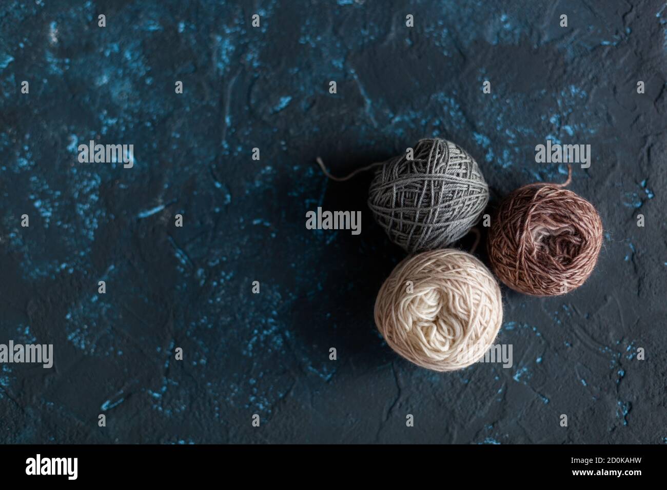 Trois boules de couleur beige brun gris pelote de fil de laine pour crochet et tricoter sur le béton de mastic de texture bleu foncé. Mettre à plat l'image avec de l'espace pour le texte. Banque D'Images