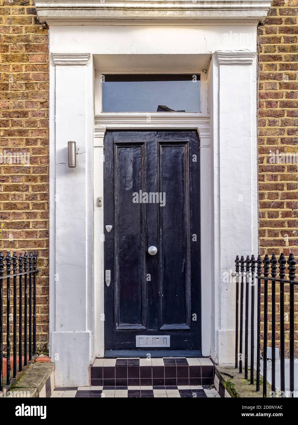 Une autre porte noire brillante à Notting Hill. Le cadre blanc contraste fortement avec les murs de briques marron foncé et le pavé de l'échiquier. Banque D'Images