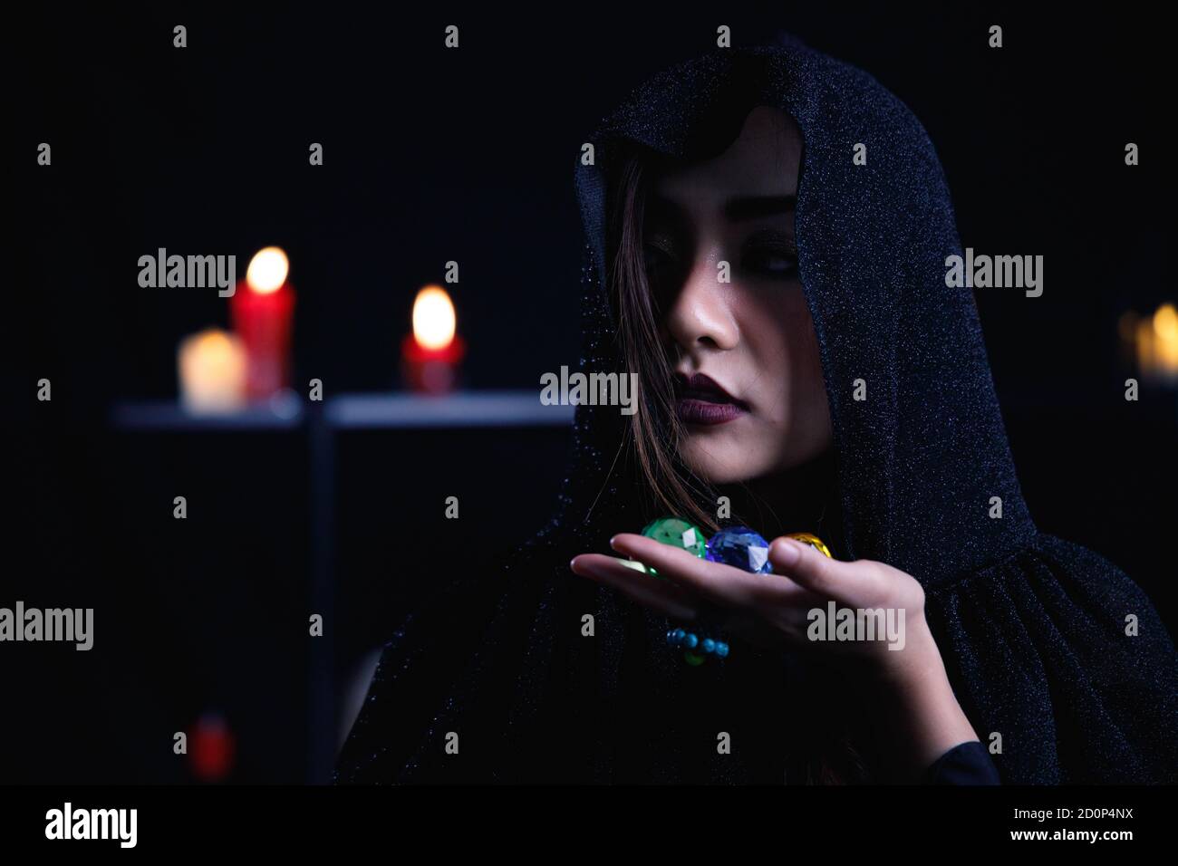 Femme mystère dans la cagoule noire tenir la gemme colorée sur fond sombre. Banque D'Images