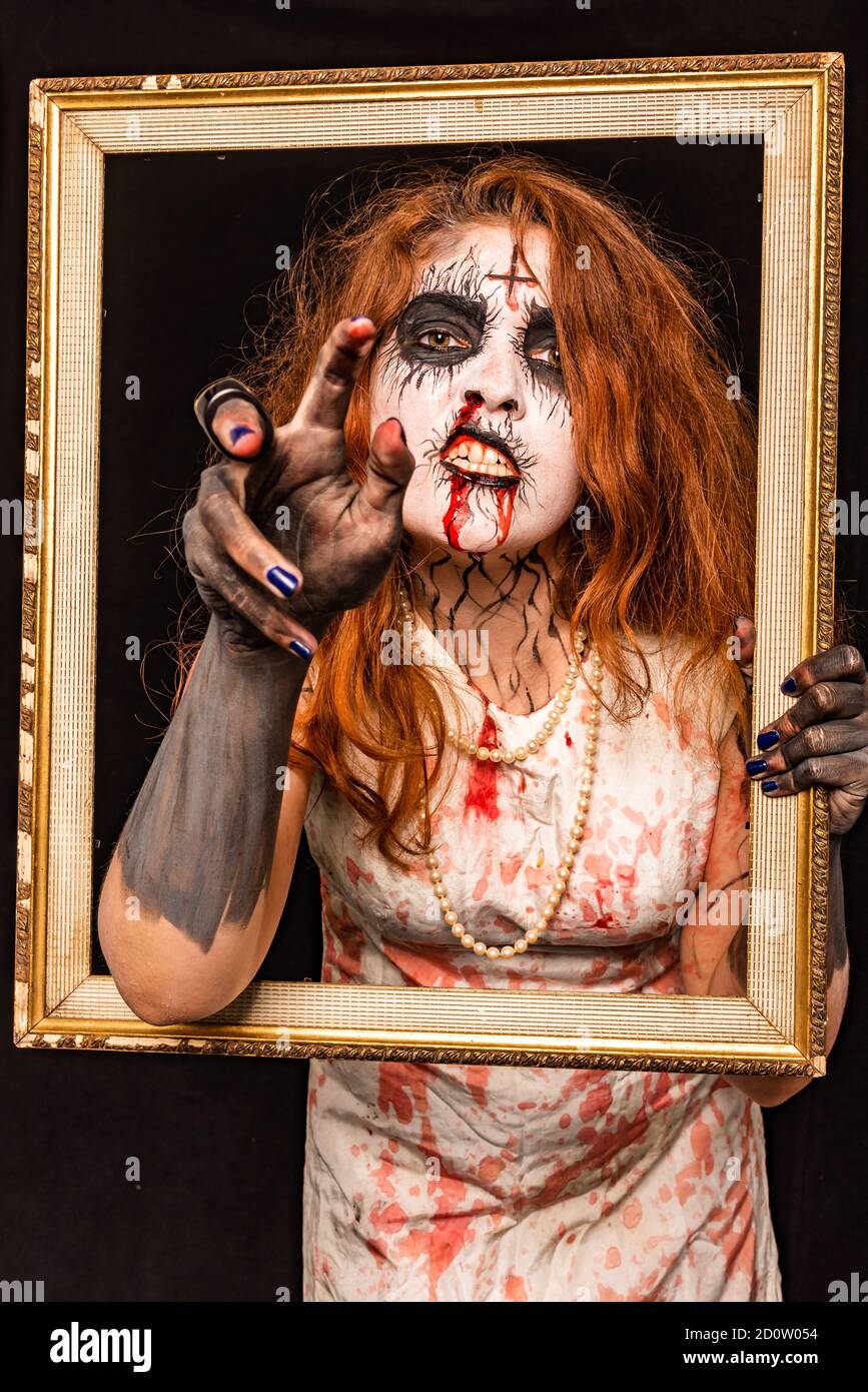 Une jeune femme à tête rouge avec un maquillage rouge et blanc pour avoir l'air créepy dans un cadre. Concept Halloween Banque D'Images