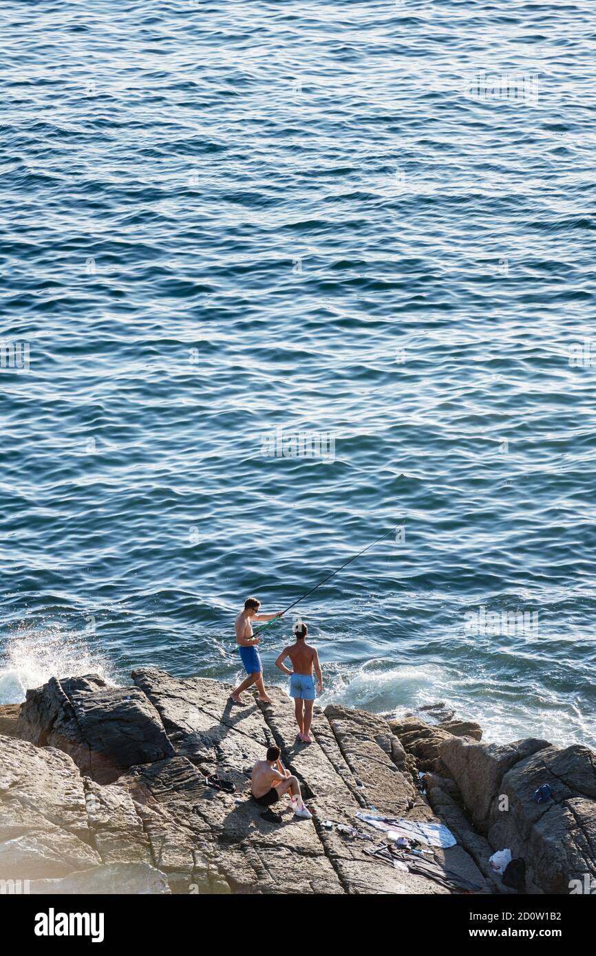 PORTONOVO, ESPAGNE - 14 AOÛT 2020 : trois jeunes pêcheurs pêchent par la mer lors d'une soirée calme et claire dans les Rias Baixas en Galice, Espagne. Banque D'Images