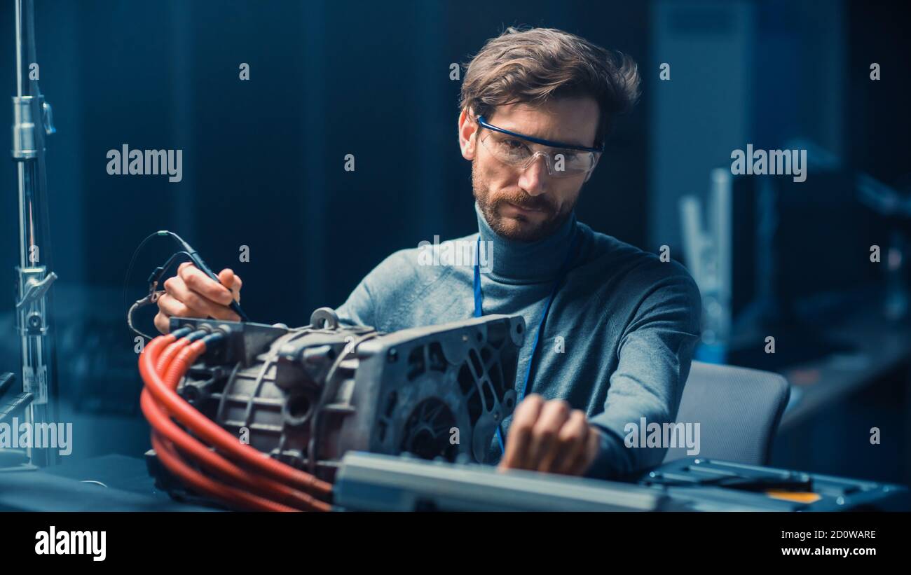 Ingénieur automobile professionnel en lunettes avec ordinateur et inspection Les outils testant un moteur électrique d'occasion dans un haut Laboratoire de technologie avec un Banque D'Images