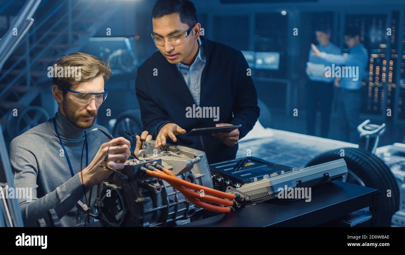 Deux ingénieurs automobiles professionnels équipés d'une tablette et d'un système d'inspection Les outils ont une conversation lors du test d'un moteur électrique Dans une haute Banque D'Images