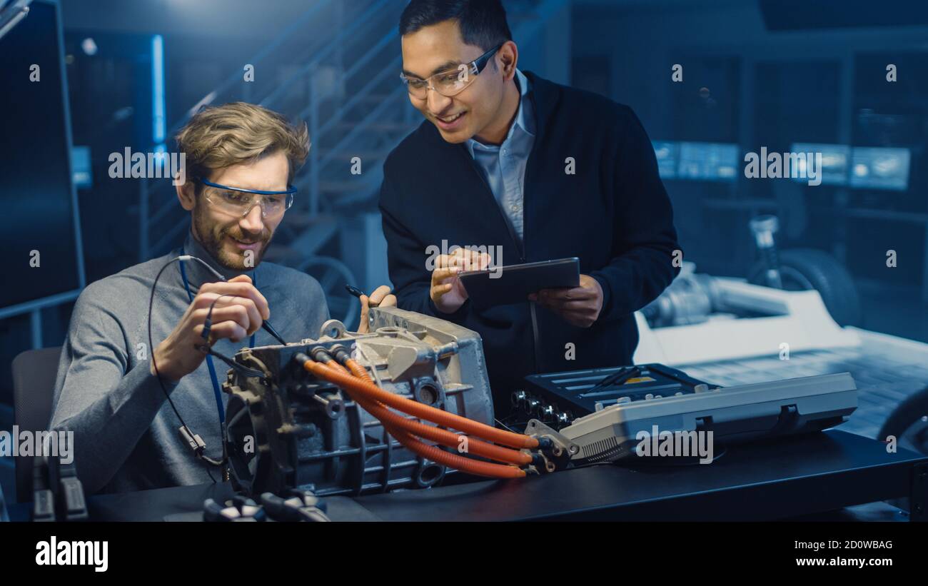 Deux ingénieurs automobiles professionnels équipés d'une tablette et d'un système d'inspection Les outils ont une conversation lors du test d'un moteur électrique Dans une haute Banque D'Images