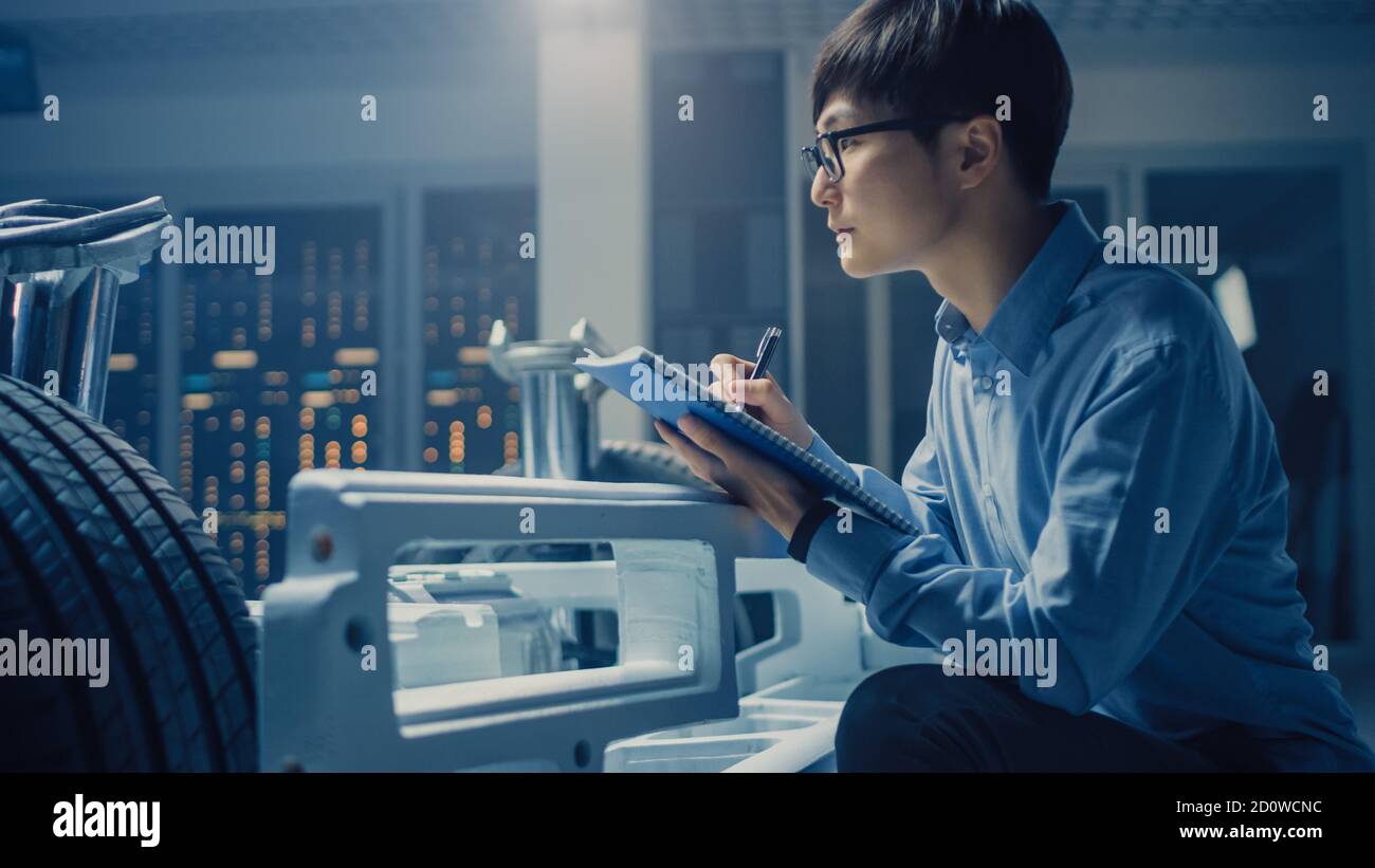 Le concepteur automobile assis à côté de la plate-forme hybride de châssis de voiture électrique, écrit des estimations et des esquisses dans le Bloc-notes. Installation avec châssis de véhicule Banque D'Images