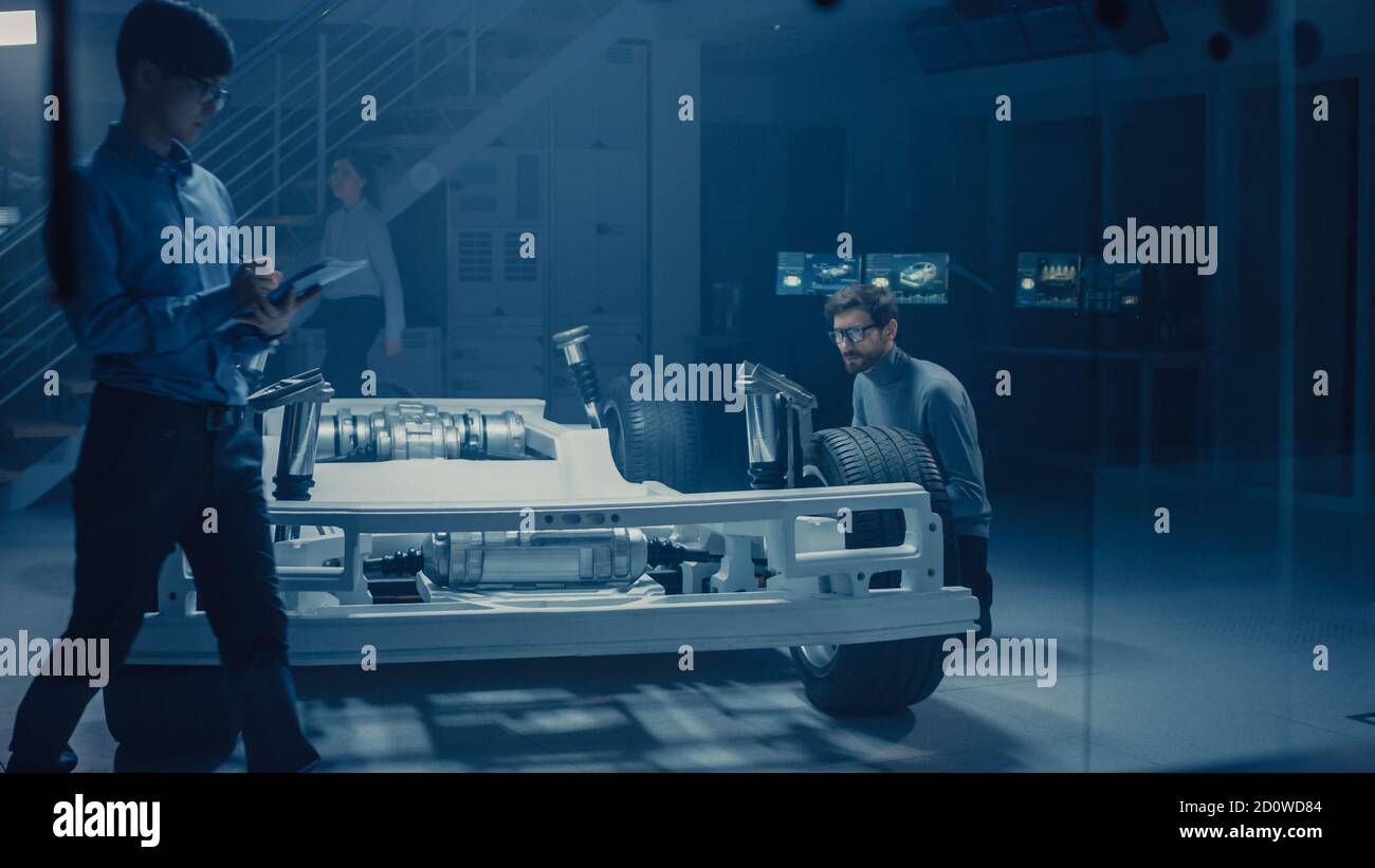 Ingénieur concepteur automobile assis à côté de la plate-forme de châssis de voiture électrique hybride, utilisant un Tablet Computer pour l'amélioration de la conception. Installation avec véhicule Banque D'Images