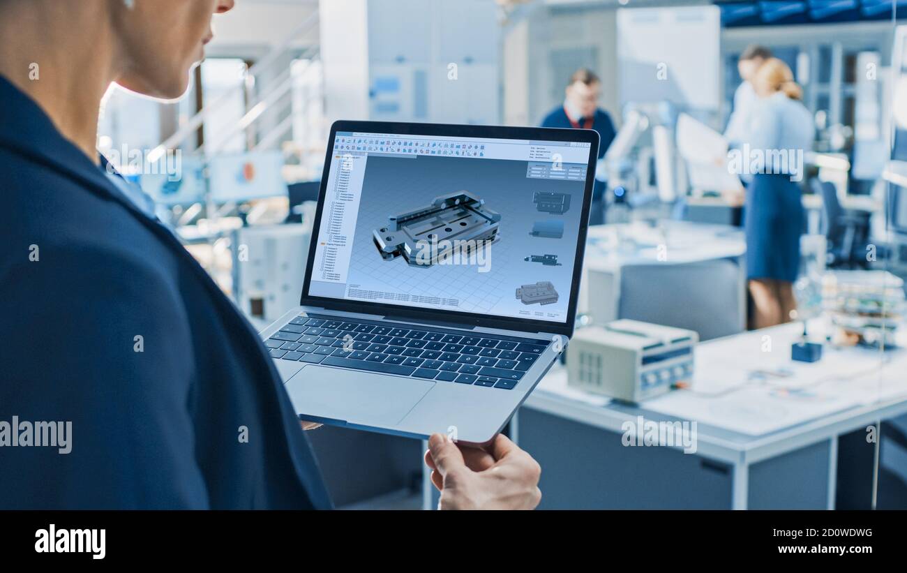 L'ingénieure féminine en robotique industrielle utilise un ordinateur portable équipé d'un logiciel de CAO pour manipuler et programmer le bras du robot pour le levage et le déplacement d'objets Banque D'Images